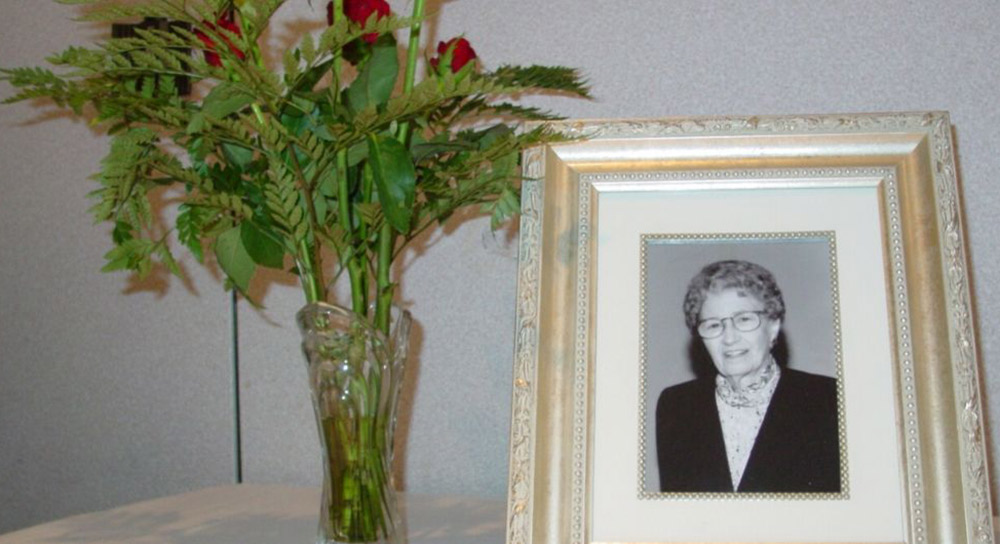 A memorial to Alice Peters with a vase of flowers and a framed picture of Alice sits on a small table.
