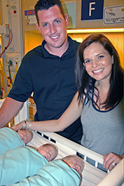 Kelsey and Fred Leyendekker stand next to their newborn triplets in the NICU