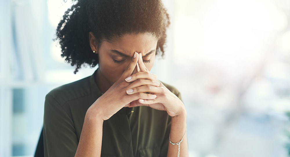 A young Black woman holds her head in her hands.