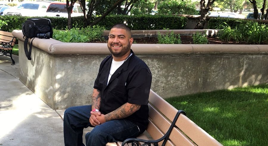 Juan Iniguez smiles and sits on a bench next to green grass