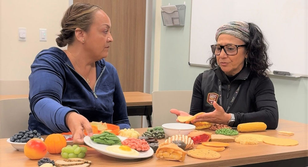 Two women sit at a table discussing the nutritious-looking variety of foods in front of them