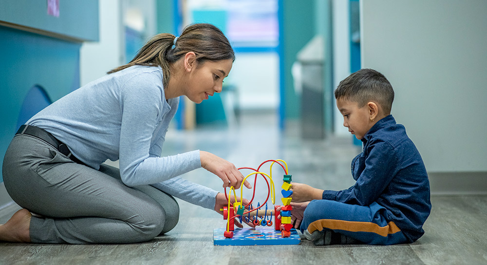 Young teacher plays on the floor with a toddler boy