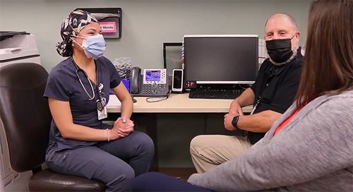 Ken Katz and Brandy Lidbeck sit opposite a female healthcare work in scrubs. They in an office setting, and all are masked. They are having a conversation.