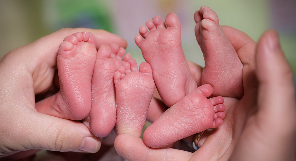 Adult hands hold three pairs of newborn baby feet