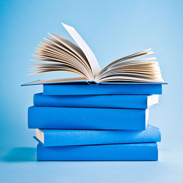 A stack of books with blue spines on a blue background. The top book is open with pages fanned upward