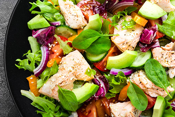 A close up image of a salad with chicken, cucumber, red onion, spinach and lettuce