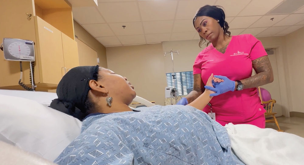 A female doula holds the hand of a pregnant mother who is in a hospital bed